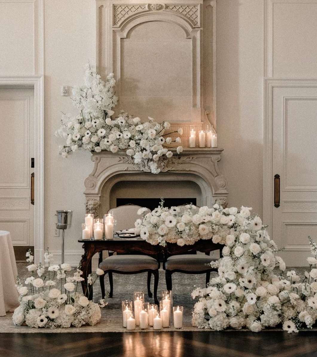 All-white sweetheart table and mantel installation of roses, anemones and gerberas with pillar candles