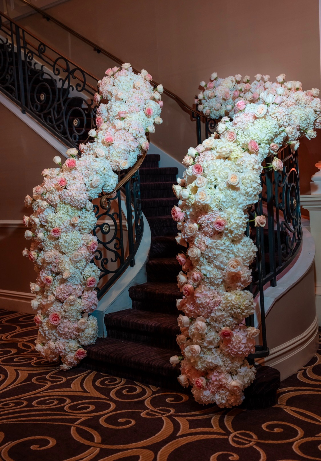 Grand staircase railings wrapped in cascading blush and ivory rose and hydrangea garlands